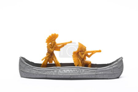 Plastic figurines of Native Americans with guns in a canoe, white background