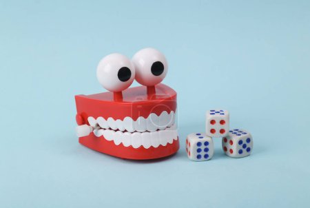 Photo for Funny toy clockwork jumping teeth with eyes and dice on blue background. - Royalty Free Image