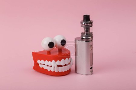 Photo for Funny toy clockwork jumping teeth with vaping device on pink background. - Royalty Free Image