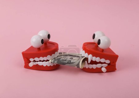 Photo for Two Funny  clockwork jumping teeth toy with dollar bills  on pink background. - Royalty Free Image