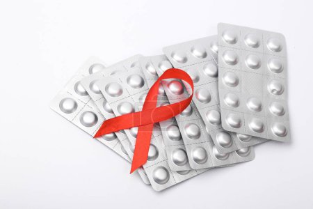 Blister pills with red ribbon symbol of the fight against AIDS on white background