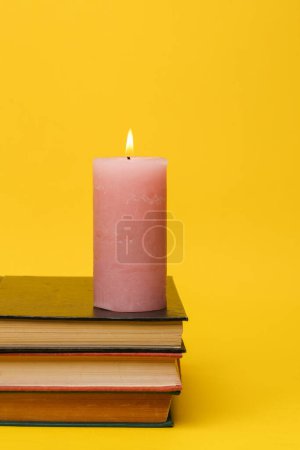 Flaming candle on a stack of books, yellow background