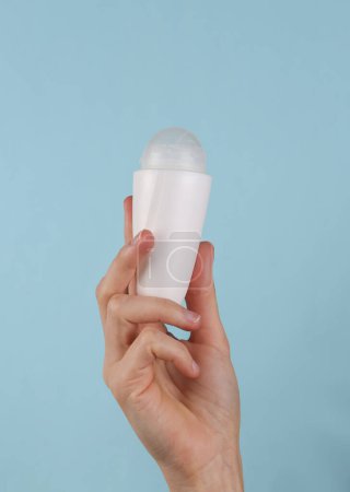 Antiperspirant roll-on stick in female hand on a blue background