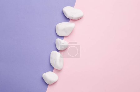 Téléchargez les photos : White pebble stones on a pink-purple background. creative composition, spa, relaxation concept - en image libre de droit