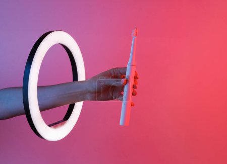 Photo for Female hand holds Ultrasonic toothbrush through led ring lamp in neon light. Creative idea. Dental health - Royalty Free Image