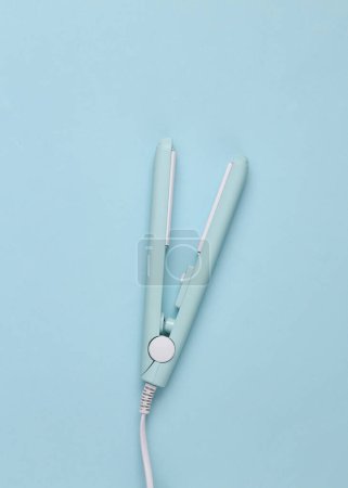 Photo for Mini hair straightener on a blue background. Top view - Royalty Free Image