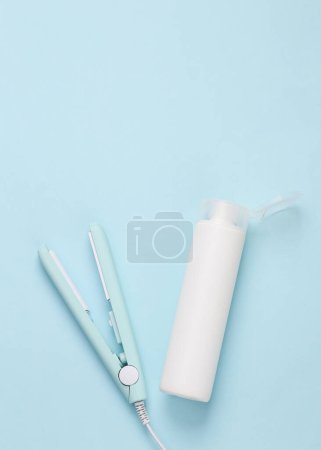 Photo for Mini hair straightener with a bottle of shampoo on a blue background. Hair style. Top view - Royalty Free Image