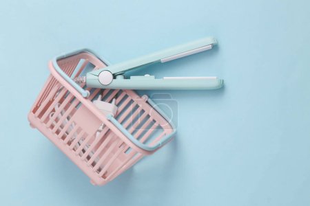 Photo for Mini hair straightener in supermarket basket on a blue background. Top view - Royalty Free Image