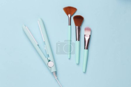 Photo for Hair iron with make-up brushes on a blue background. Top view. Flat lay - Royalty Free Image