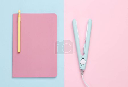 Photo for Mini hair straightener with notebook on a blue pink background. Top view - Royalty Free Image