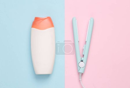Photo for Mini hair straightener with a bottle of shampoo on a blue pink background. Hair style. Top view - Royalty Free Image