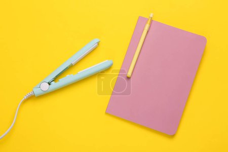 Photo for Mini hair straightener with notebook on a yellow background. Top view - Royalty Free Image
