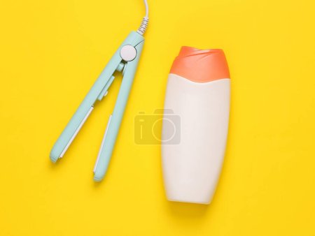 Photo for Mini hair straightener with a bottle of shampoo on yellow background. Hair style. Top view - Royalty Free Image