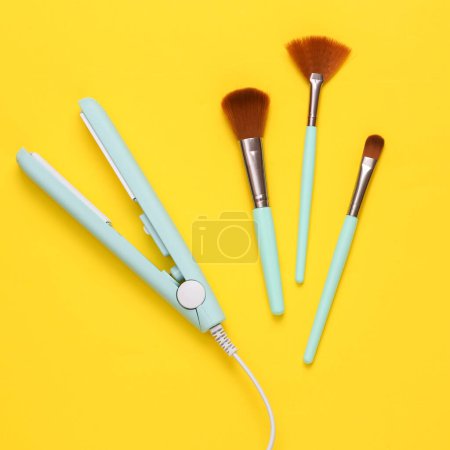 Photo for Hair straightener with make-up brushes on yellow background. Top view. Flat lay - Royalty Free Image