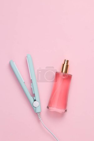 Photo for Hair straightener with perfume bottle on a pink background - Royalty Free Image