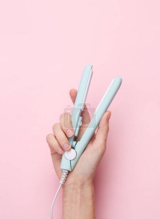 Photo for Mini hair straightener in a female hand on a pink background - Royalty Free Image