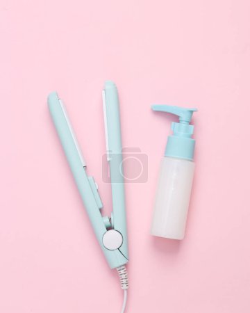 Photo for Hair straightener with cream bottle on a pink background - Royalty Free Image