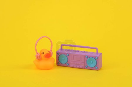 Foto de Pato de goma con auriculares y reproductor de audio boombox sobre fondo amarillo. Concepto musical - Imagen libre de derechos