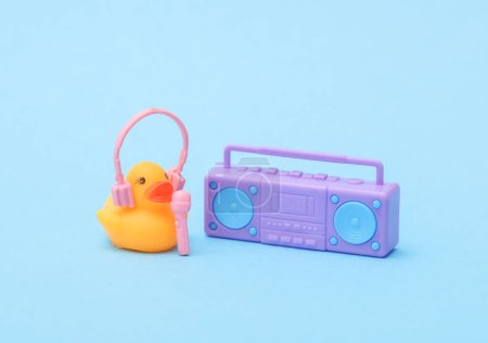 Foto de Pato de goma con auriculares y reproductor de audio boombox sobre fondo azul. Concepto musical - Imagen libre de derechos