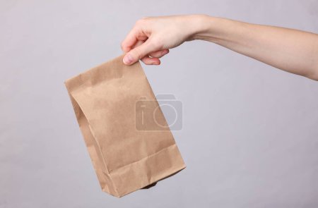 Téléchargez les photos : Main féminine tenant paquet de produits artisanaux sur fond gris - en image libre de droit