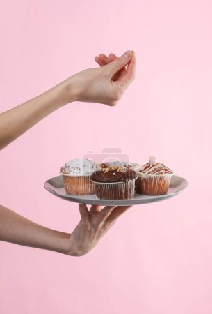 Téléchargez les photos : Main de femme tenant une assiette de cupcakes sur un fond rose - en image libre de droit