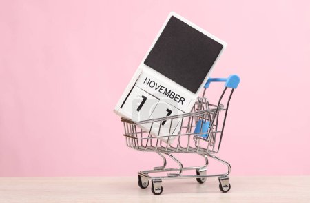 Photo for Calendar with the date november 11 in mini supermarket trolley on the table, pink background. World Shopping Day. 11.11. - Royalty Free Image