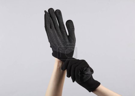 Foto de Las manos femeninas se ponen guantes de tela de trabajo negro sobre un fondo gris - Imagen libre de derechos