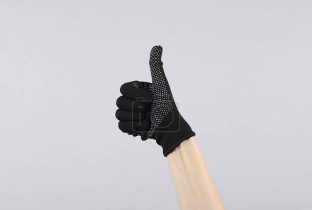 Foto de La mano de la mujer en un guante de tela de trabajo muestra un pulgar hacia arriba sobre un fondo gris - Imagen libre de derechos