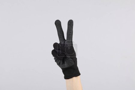 Foto de Mano femenina en un guante de tela de trabajo muestra con los dedos v símbolo sobre un fondo gris - Imagen libre de derechos