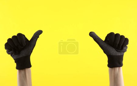 Foto de Las manos femeninas en guantes de tela de trabajo muestran los dedos hacia arriba en el espacio para el texto, sobre fondo amarillo - Imagen libre de derechos
