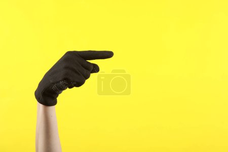 Foto de Mano femenina en guante de tela de trabajo muestra el dedo en el espacio para el texto, sobre fondo amarillo - Imagen libre de derechos