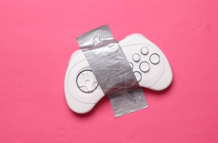 Photo for White retro gamepad fixed with adhesive tape on a pink background. Conceptual pop, video game - Royalty Free Image