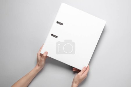 Téléchargez les photos : Mains féminines tenant un dossier de reliure blanche sur un fond gris - en image libre de droit