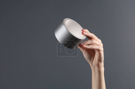 Téléchargez les photos : Main tenant du ruban adhésif sur fond gris - en image libre de droit
