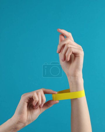 Photo for Female hand with a yellow paper bracelet on a blue background - Royalty Free Image