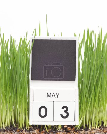 Wooden block calendar with date may 3 on green grass isolated on white background. Springtime, planning