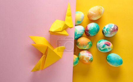 Multicolored Easter eggs, origami dove and rabbit on yellow pink background.