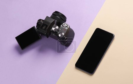 Modern digital camera with flip screen and smartphone on pastel background