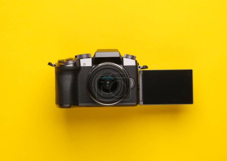 Modern digital camera with flip screen on yellow background