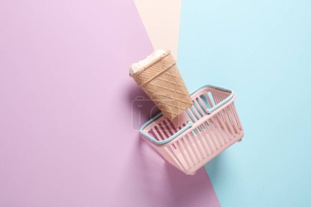 Téléchargez les photos : Cône de gaufre à la crème glacée en mini panier de supermarché sur fond pastel - en image libre de droit