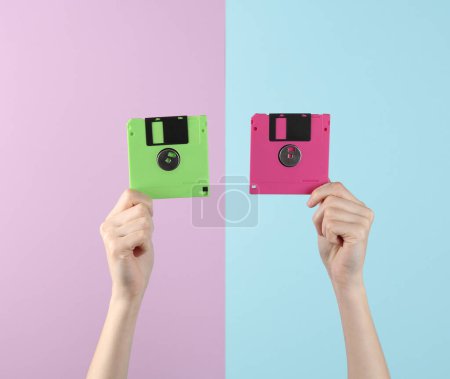 Téléchargez les photos : Les mains féminines tiennent deux disquettes obsolètes colorées sur un fond pastel bleu-rose. Rétro années 80 - en image libre de droit