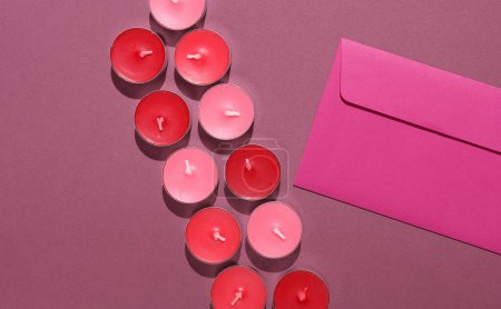 Envelope with Aroma tea candles on burgundy background. Romantic, love concept. Top view.