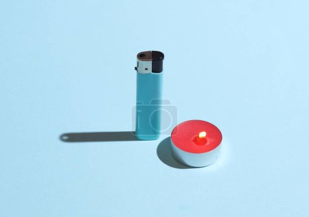 Red and pink Aroma tea candle and lighter on blue background. Creative layout, minimalism