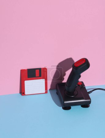 Téléchargez les photos : Disque souple et joystick sur fond bleu rose. Rétro années 80. Un jeu vidéo. Une technologie obsolète. Mise en page créative, minimalisme, nature morte minimale à la mode - en image libre de droit