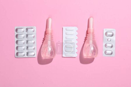 Women's health concept. Vaginal enemas, pills and pink awareness ribbon on pink background. Flat lay