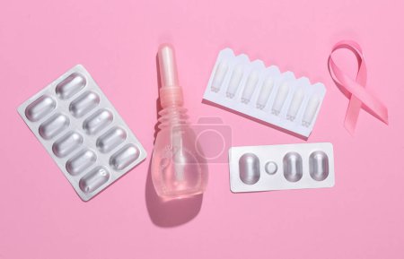 Concepto de salud de la mujer. Enemas vaginales, pastillas y cinta rosa sobre fondo rosa. Puesta plana