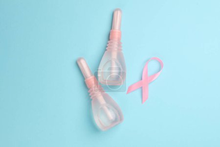 Two vaginal enemas and a pink awareness ribbon on blue background. Women's health