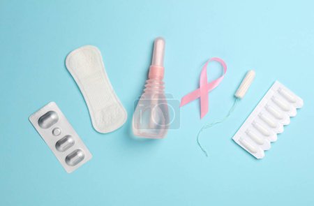 Women's health concept. Vaginal enemas, pad, tampon and pink awareness ribbon on blue background. Flat lay