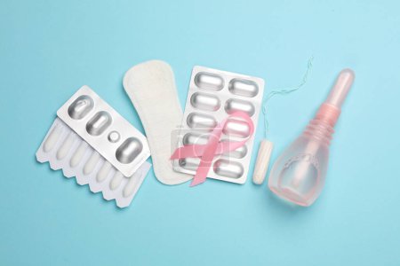 Women's health concept. Vaginal enemas, pad, tampon, pills and pink awareness ribbon on blue background. Flat lay.