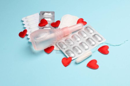 Women's health concept. Vaginal enema, Pad, tampon and pink awareness ribbon, pills, red hearts on blue background.